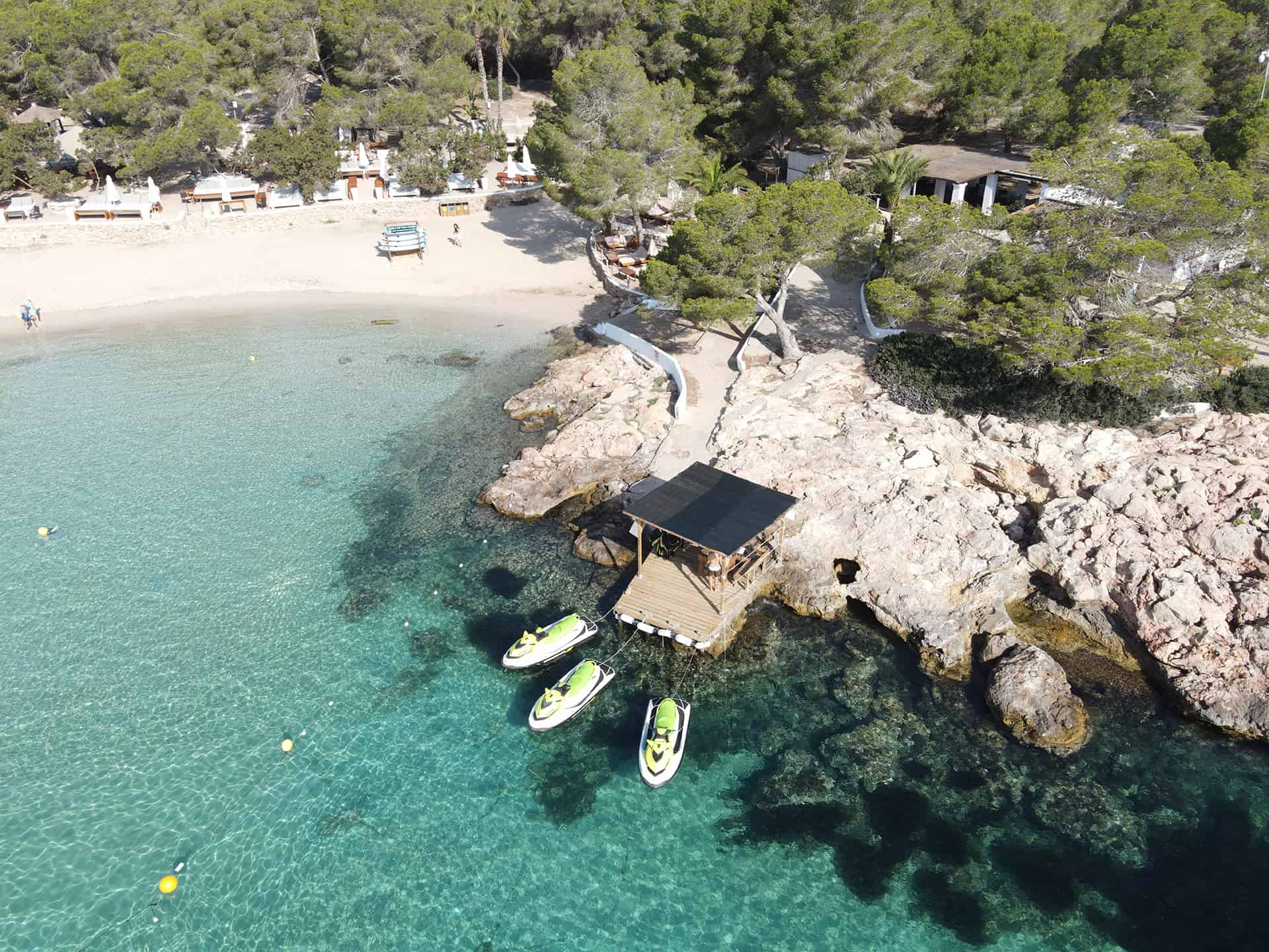 Aerial view of three jet skis docked in a turquoise cove in Ibiza